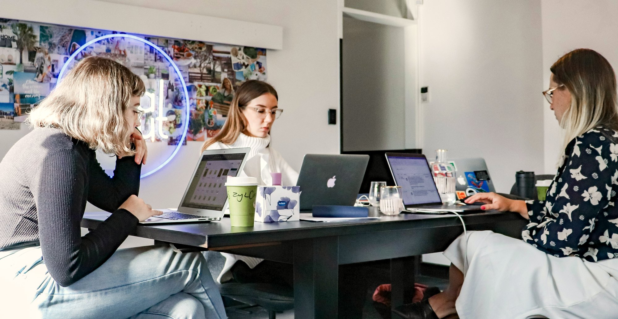 Three people working together at a shared table, laptops open.